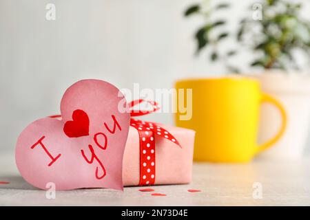 Heart shaped greeting card with phrase I Love You near gift box on table Stock Photo