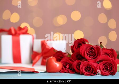 Beautiful red roses, decorative heart, love letter and gift boxes on table against blurred lights, space for text. St. Valentine's day celebration Stock Photo