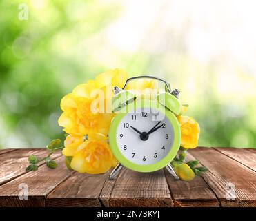 Alarm clock and spring flowers on wooden table. Time change Stock Photo