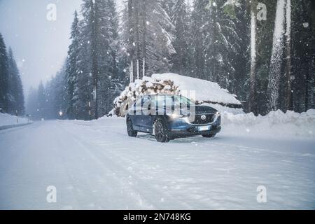 Italy, Veneto, Belluno, a Mazda Motor Corp. CX-30 crossover sport utility vehicle (SUV) on a mountain road in winter during a snowfall, Dolomites Stock Photo