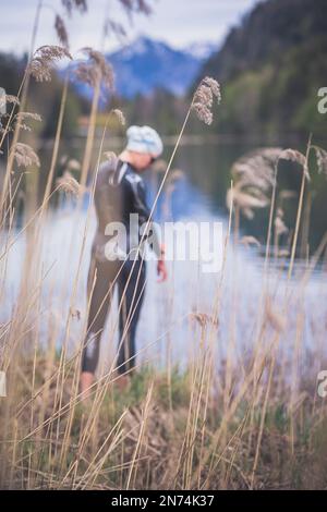 Professional triathlete before swimming, training in a clear mountain lake in Allgäu, Alatsee, Bavaria, Germany Stock Photo