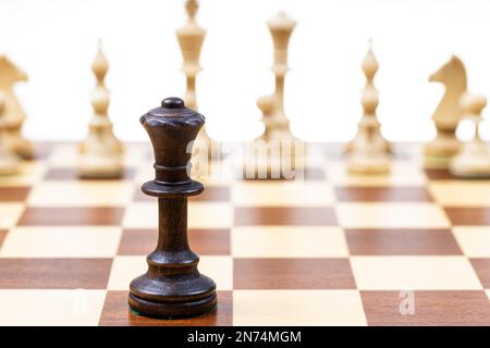 black queen against white chess figures in background on wooden chessboard close up (focus on queen) Stock Photo
