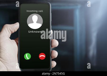 Male hand holding mobile phone showing incoming call from an unknown caller on the screen, with buttons to answer or reject. Possible scammer or spam Stock Photo