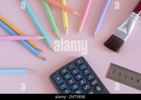 Pastel colored pencils with a brush and a calculator, top view on pink background, back to school concept Stock Photo