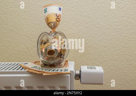 Glass piggy bank filled with euro coins, 50 euro bills on Heizköper, WLAN radiator thermostat FRITZ! DECT 302, display shows 19°C., symbol image, savi Stock Photo
