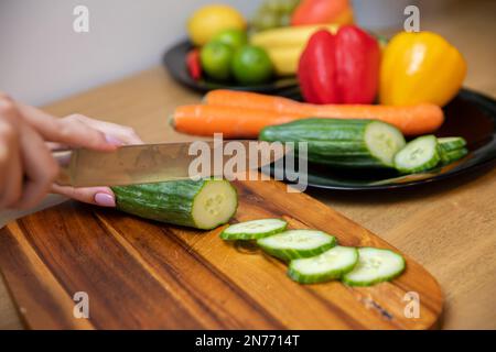 female hands slicing a cucumber on a wooden cutting board Stock Photo