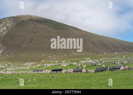 19th century stone cottages, the remains of older blackhouses and drystone storage chambers (cleitean) below the peak of Conachair on Hirta, St Kilda Stock Photo