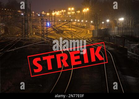 German text Streik (meaning strike) over shiny and curving railway tracks at night in a cargo freight station, copy space, selected focus Stock Photo