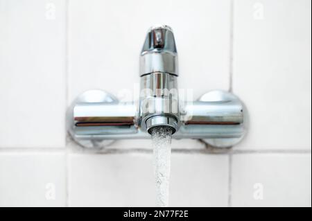 Bath fitting or tap with running water on a white tiled wall in an older bathroom, copy space, selected focus, very narrow depth of field Stock Photo