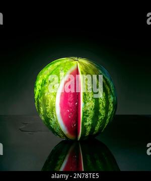 Watermelon with a slice removed, with reflection, isolated on dark background Stock Photo