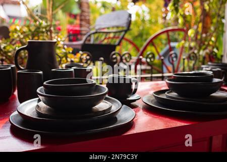 A dining set painted black rests on a red table outside with green vegiation serving as a backdrop. Stock Photo