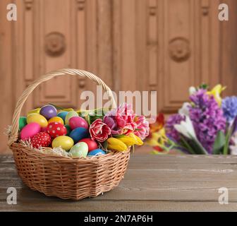 Wicker basket with bright painted Easter eggs on wooden table indoors, space for text Stock Photo