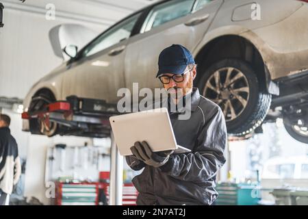 young serviceman checking car diagnostics with a laptop, car in the background medium shot. High quality photo Stock Photo