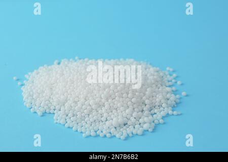 Pellets of ammonium nitrate on light blue background, space for text. Mineral fertilizer Stock Photo