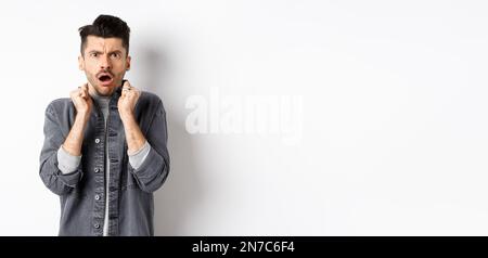 Shocked young man look confused and offended, gasping and frowning at camera, hear bad news, standing on white background Stock Photo