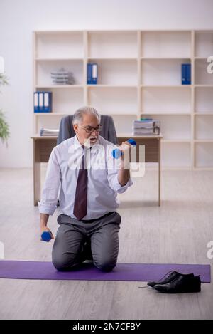 Old employee doing sport exercises during break Stock Photo