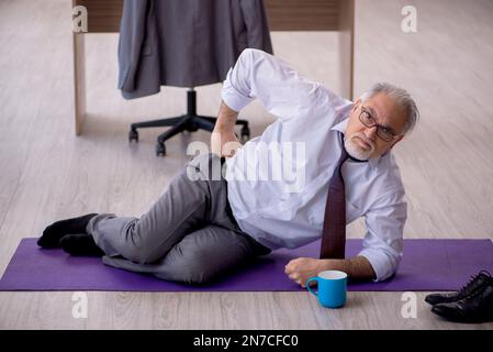 Old employee doing sport exercises during break Stock Photo