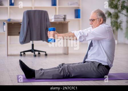 Old employee doing sport exercises during break Stock Photo