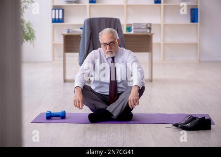 Old employee doing sport exercises during break Stock Photo