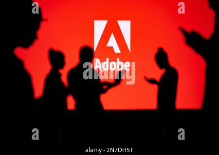 JAPAN, TOKYO. JANUARY 30, 2023: Adobe. Collaborating for Innovation: Silhouetted Web Developers in Action with Company Logo in Background Stock Photo