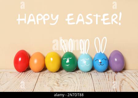 Several eggs with drawn faces and ears as Easter bunnies among others on white wooden table against beige background Stock Photo