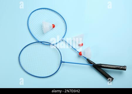 Rackets and shuttlecocks on light blue background, flat lay. Badminton equipment Stock Photo