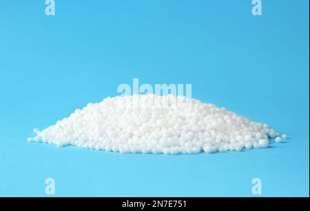 Pellets of ammonium nitrate on light blue background, space for text. Mineral fertilizer Stock Photo