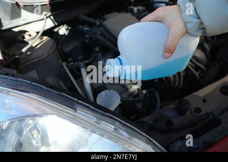 Woman pouring antifreeze from plastic canister into windshield washer fluid reservoir, closeup Stock Photo
