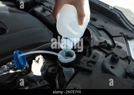 Man pouring antifreeze from plastic canister into windshield washer fluid reservoir, closeup Stock Photo