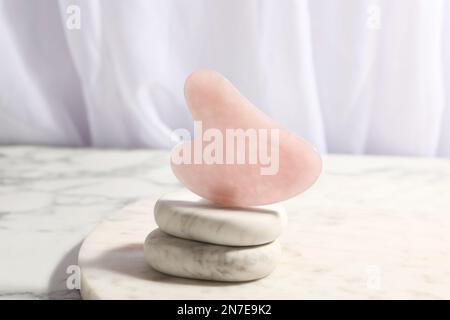 Rose quartz gua sha tool and spa stones on white marble table Stock Photo