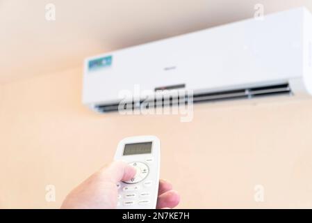 Hand with remote control directed on air conditioner. Climate control indoor concept Stock Photo