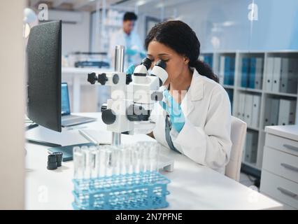 Every new day presents a new opportunity. a young female lab worker analysing samples through a microscope. Stock Photo