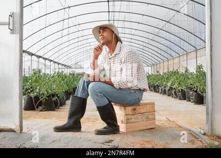 Thinking of the best plans for his sustainable agribusiness. a young man looking thoughtful while writing notes in a greenhouse on a farm. Stock Photo