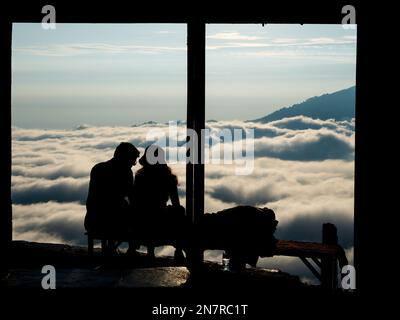 A young couple sitting on a bench above clouds in Bali Stock Photo