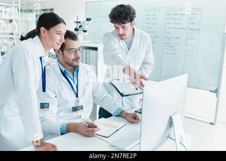 Modifying their theory. a group of scientists working together on a computer in a lab. Stock Photo