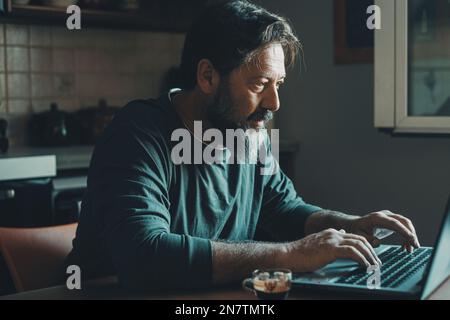 Mature male workaholic involved in work overtime, type report letter on laptop, search data at web. Ambitious young man in smart working develop caree Stock Photo