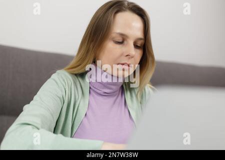 Focused white woman working on computer at home. Serious adult female person doing distant work online Stock Photo
