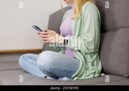 Adult woman sitting on couch and typing a message on smart phone. Unrecognizable white female person using modern mobile phone app at home Stock Photo