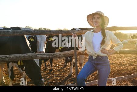 Young woman with shovel standing near cow pen on farm. Animal husbandry Stock Photo