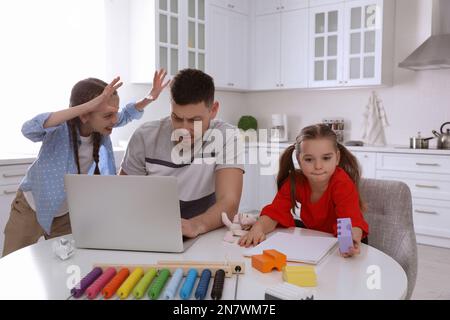 Children disturbing stressed man in kitchen. Working from home during quarantine Stock Photo