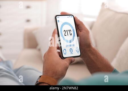 Man using smartphone to control heating system in house, closeup Stock Photo