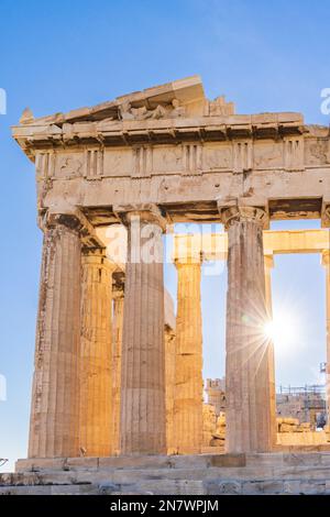 Sun hiding behind the columns of the Parthenon temple at Acropolis site on a sunny evening in Athens Greece Stock Photo