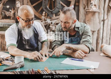 master of leather tailor teaching and training young man for making handcraft leather pouch Stock Photo