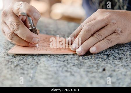 closeup hand working process leather handcraft in the leather workshop. Man holding crafting tool and working. He is sewing hammer to make a walet. Ta Stock Photo