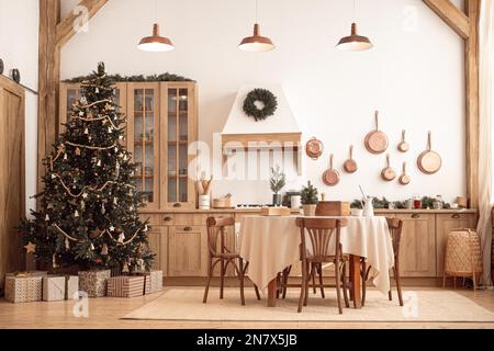 Modern, light, festive, cozy kitchen interior with Christmas and New Year decorations, kitchen table, utensils, copper pans on wall and big Christmas Stock Photo