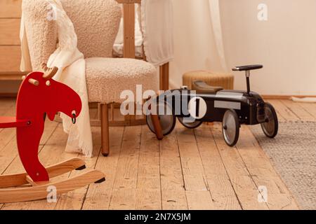 Stylish spacious Scandinavian newborn baby nursery room with toys, bed, playpen, chair, wooden rocking horse, car. Modern interior with beige light Stock Photo