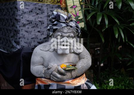 The gate guard statue is made of stone covered by Balinese sacred cloth and udeng called Dwarapala is guarding Canang Sari as offerings Stock Photo