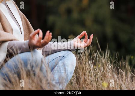 Woman practicing yoga exercise in lotus position. Meditation outdoors. Selective focus on hand Stock Photo