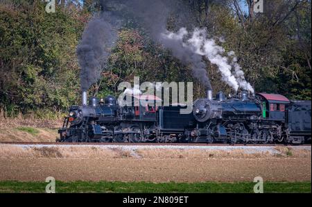 A View of Two Steam Engines, blowing Smoke and Steam Warming Up Next to Each Other on a Sunny Day Stock Photo