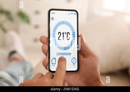 Man using smartphone to control heating system in house, closeup Stock Photo